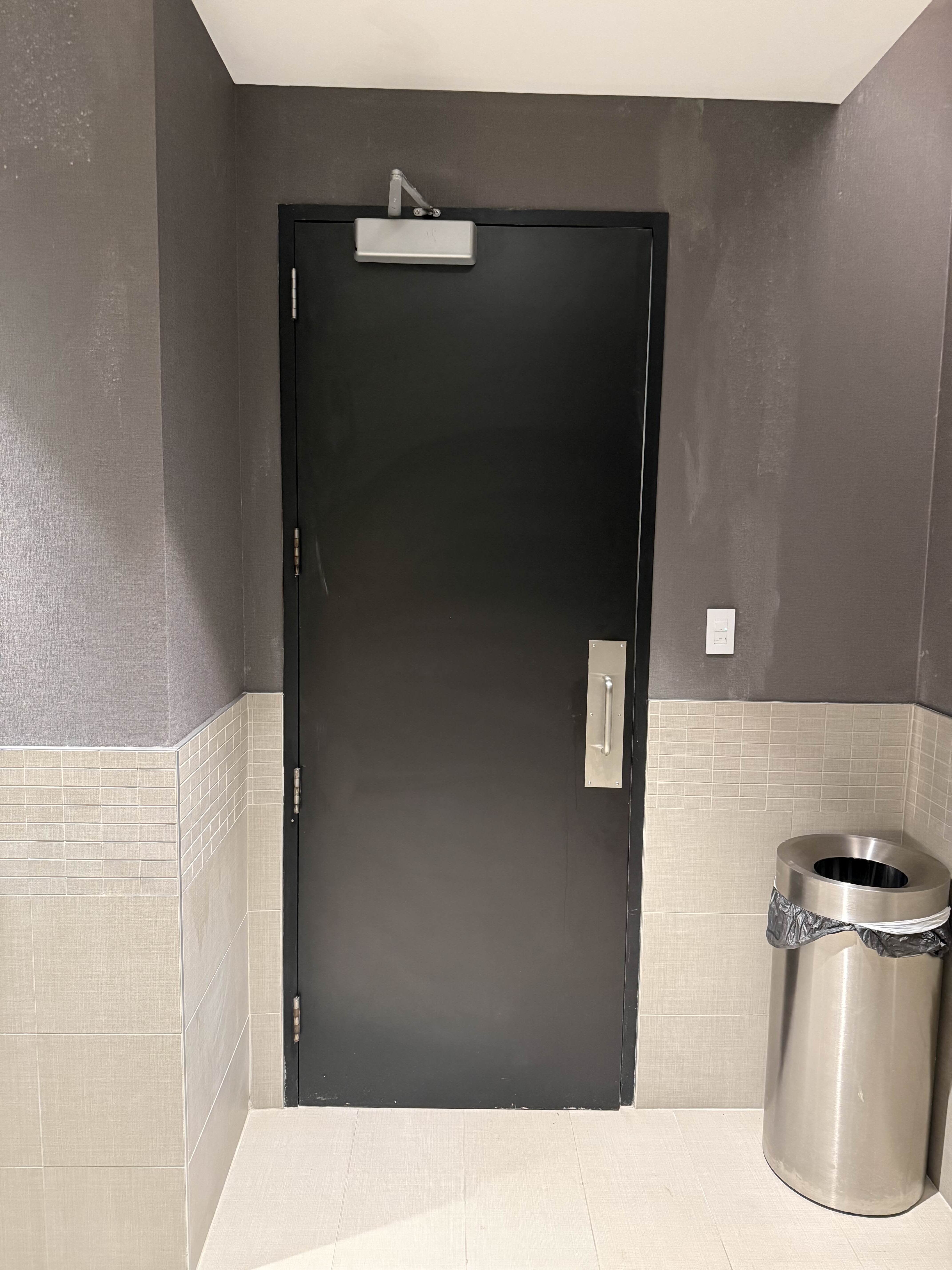 Interior of restroom door before access control — only a door closer, no ADA push button or mag lock
