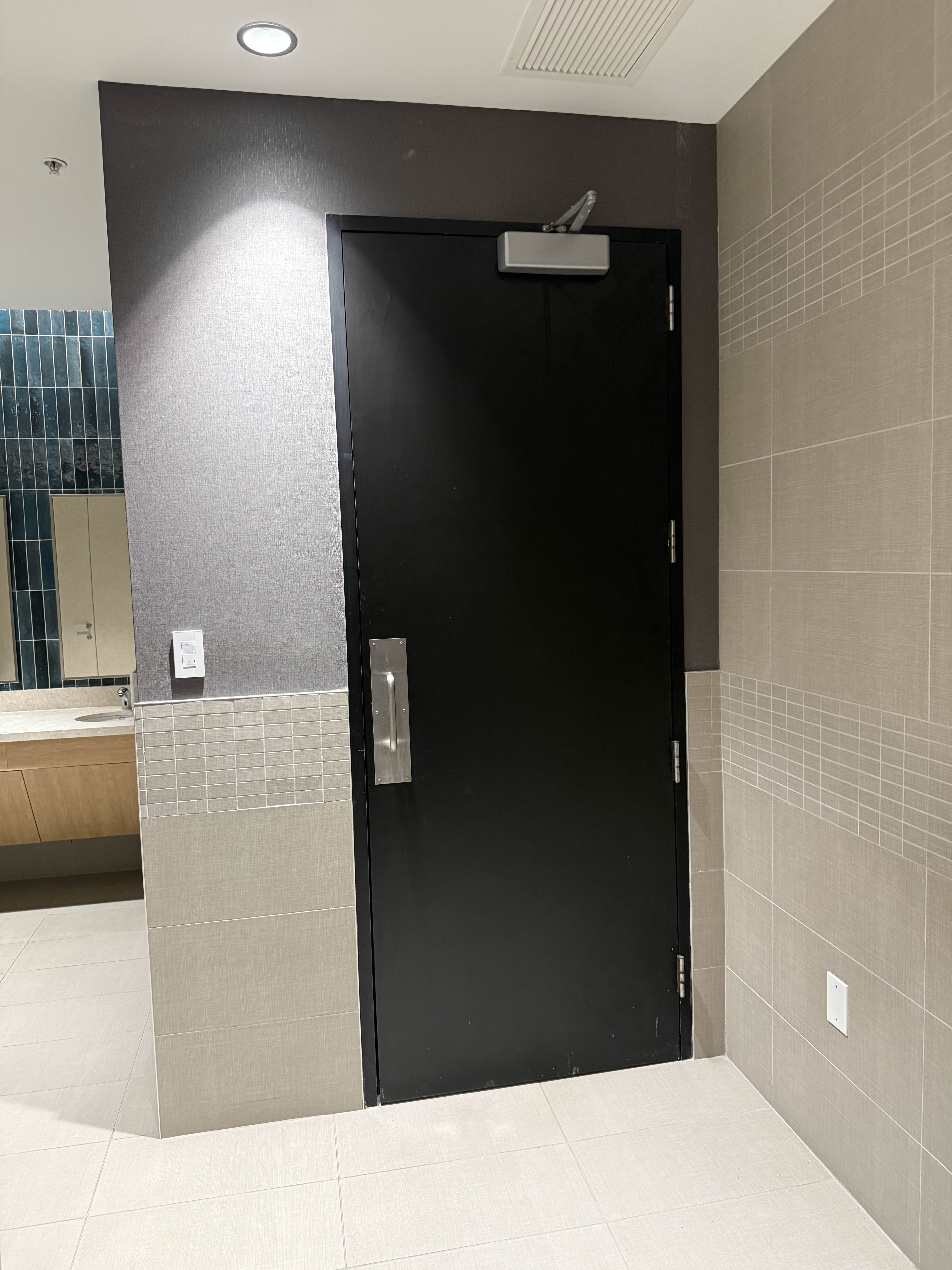 Restroom interior before access control installation — door closer and pull handle, no electronic access hardware