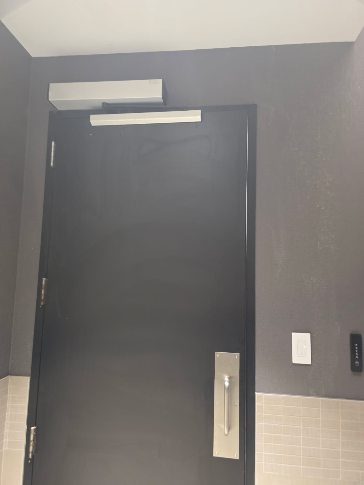 Magnetic door lock and door closer installed above commercial restroom door in Dallas